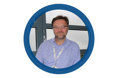 Pictured Gordon Beattie dark brown hair with brown/ grey beard stubble and gold top (bottom frameless) spectacles. Gordon is wearing a pale blue and white dog-tooth checked shirt, open with NSS lanyard