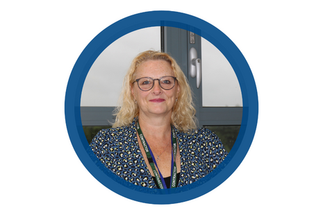 Pictured Julie Critchley blonde shoulder length curly hair wearing dark blue framed glasses, dark pink lipstick - Blue beige and yellow cheetah print dress jacket with black top - silver necklace with love knot diamante pendant